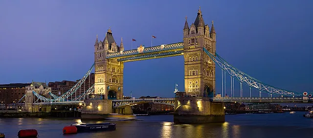Tower Bridge at dusk with its lights on, reflected in the Thames under a deep blue sky